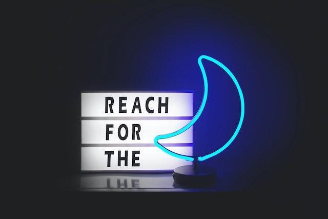 Neon signs “reach for the” and “moon”.
