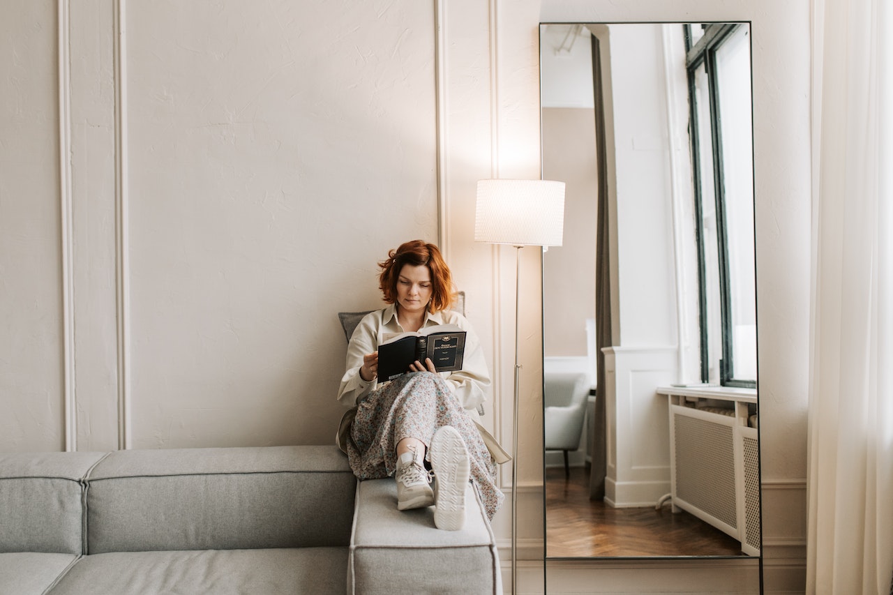 A red-haired woman reading a book next to the lamp.